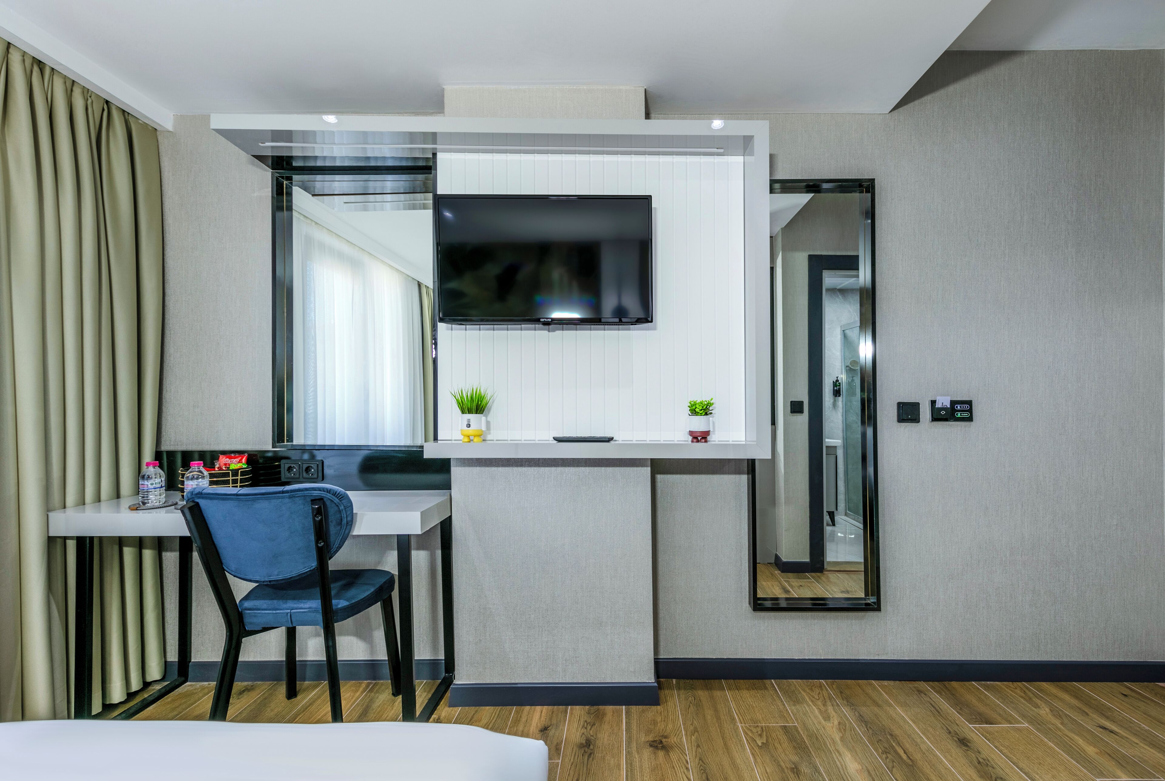 A modern hotel room with a desk, chair, TV, and a small plant.