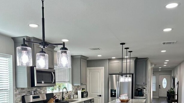 Une cuisine moderne dotée d’un îlot central, d’appareils électroménagers en acier inoxydable et de luminaires suspendus.