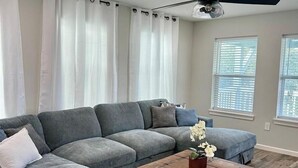 Un salon avec un canapé d’angle, une table basse en bois et un ventilateur de plafond.