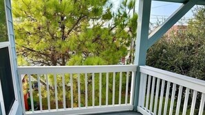 Une véranda couverte avec une balustrade blanche, un plancher en bois et une vue sur des arbres et des arbustes verdoyants.