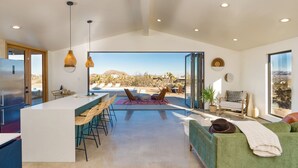 A modern kitchen with a large island, bar stools, and a view of a desert landscape through large windows. - Luxury Spa home w/ Entertainers Pool, hot tub & fire pits! (Yucca Valley)