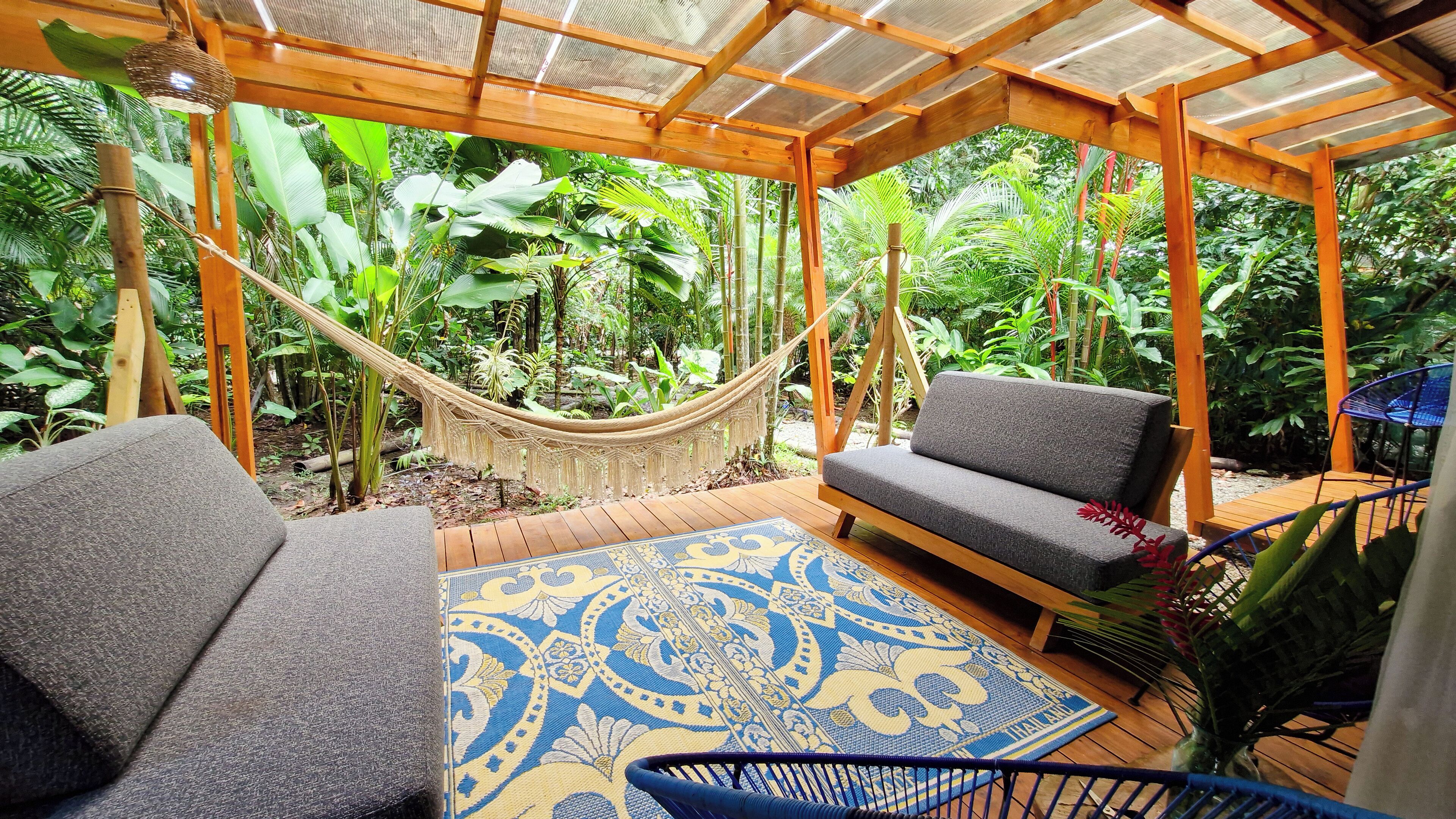 A wooden deck with a hammock, two grey sofas, and a blue patterned rug.