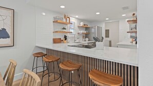 Una cucina moderna con mobili bianchi, sgabelli da bar in legno e mensole a incasso.