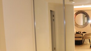 A room with a large mirror, a door leading to another room, and a dining area with chairs and a table.