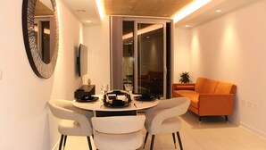 A modern dining area with a round table, four chairs, a television, and a sliding glass door leading to a balcony.