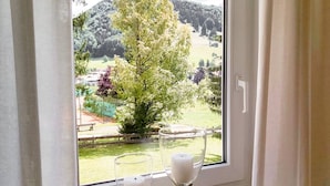 Ein Fenster mit Blick auf eine grüne Landschaft, eine Bank und ein Glasschalenkerzenhalter.