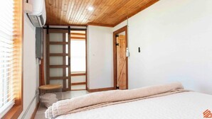 A bedroom with a wooden ceiling, a bed with a beige blanket, a wooden door, and a window with blinds. - Quaint Cottage Downtown Buckner (Buckner)