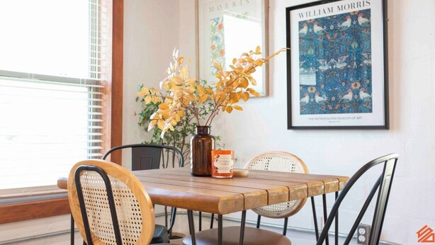A dining area with a wooden table, four chairs, a vase with yellow flowers, and a framed artwork on the wall. - Quaint Cottage Downtown Buckner (Buckner)