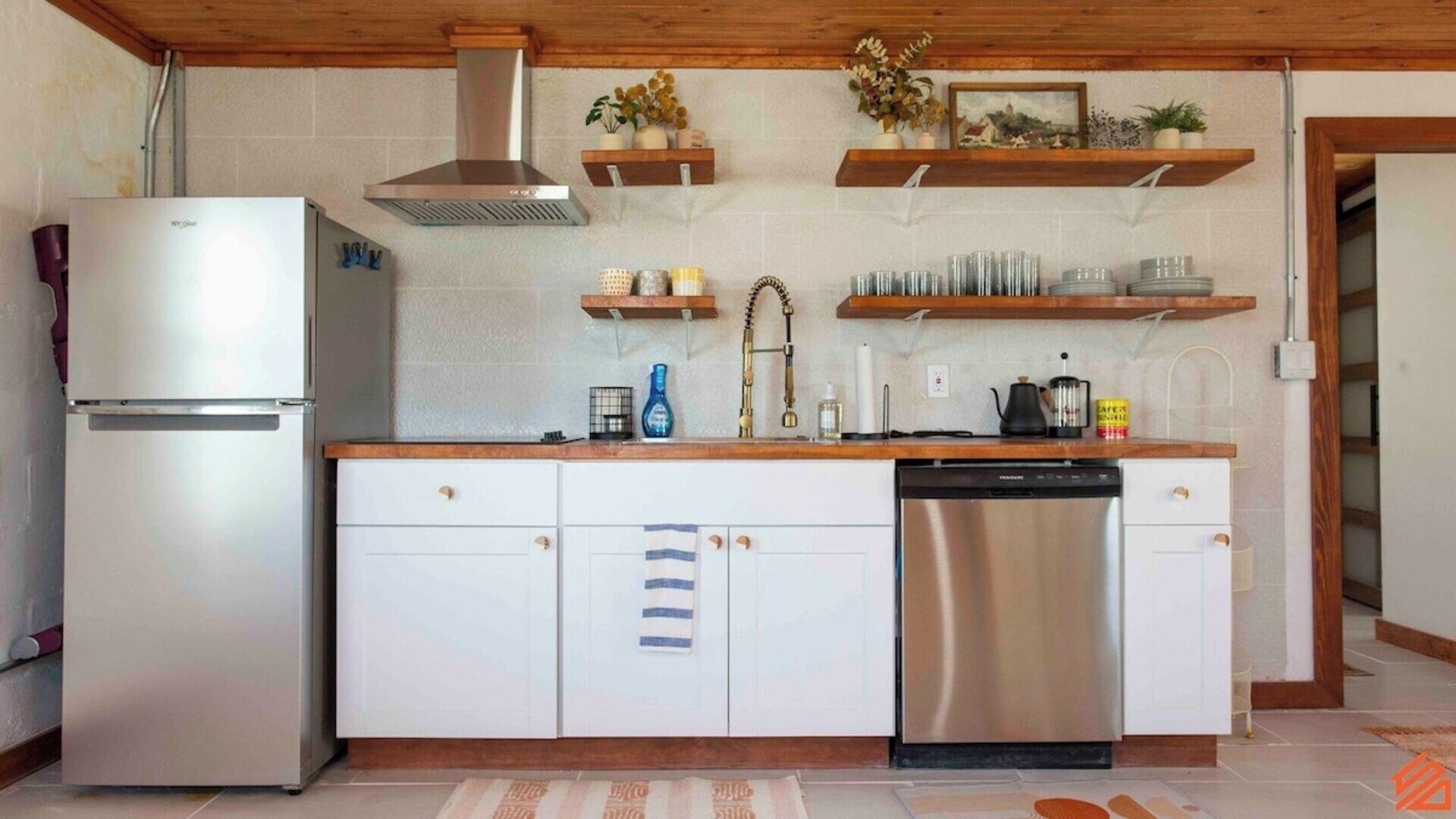 Een compacte keuken met een roestvrijstalen koelkast, een vaatwasser, houten kastjes en een betegelde spatwand.