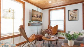 A living room with a wooden ceiling, a mounted TV, a sofa, a coffee table, and a patterned rug. - Quaint Cottage Downtown Buckner (Buckner)