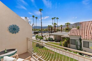 A balcony with a view of a parking lot, palm trees, and a mountain in the background.