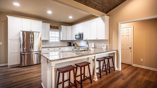 A modern kitchen with white cabinets, a stainless steel refrigerator, a granite countertop, and wooden stools. - The Red Door Cottage (Dahlonega)
