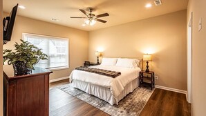 A bedroom with a bed, bedside lamps, a ceiling fan, a wooden desk, and a potted plant. - The Red Door Cottage (Dahlonega)