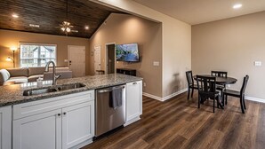 A modern kitchen with a large island, built-in appliances, and a dining area with a wooden table and chairs. - The Red Door Cottage (Dahlonega)