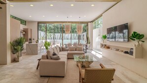 A spacious living area with a large sofa, a coffee table, and a TV mounted on the wall. There are potted plants and a dining area visible. - Modern 4-bedroom  4- bathroom villa with private pool in Tulum.  (Tulum)