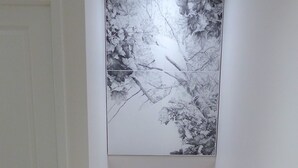 Uma grande obra de arte monocromática de uma árvore com um pássaro no galho, fixada numa parede branca.