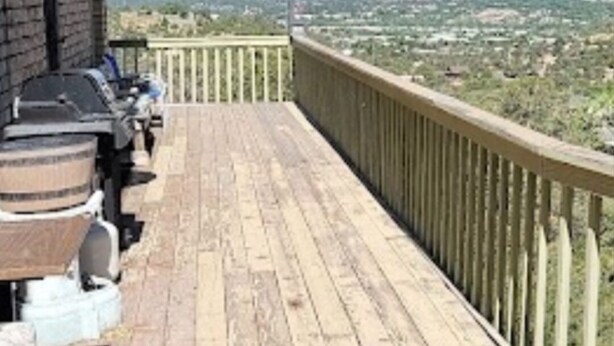 Une terrasse en bois dotée d’une rambarde, offrant une vue sur un paysage avec des montagnes lointaines et un ciel dégagé.