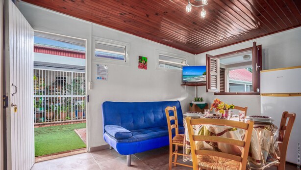 Una sala de estar acogedora con un sofá azul, sillas de madera, una mesa de comedor con mantel y un televisor en la pared.