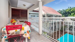 Un balcón con mesa lista para comer, una silla y vistas a una piscina y edificios al fondo.