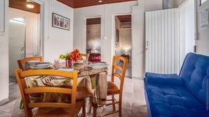 Un comedor con mesa de madera, sillas y un sofá azul. Hay cuadros en la pared y una puerta que conduce a otra habitación.