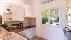 A modern kitchen with white cabinetry, a built-in oven, and a window with a view of greenery. - Casa Vinti - Vue mer et montagne, piscine (Grosseto-Prugna)