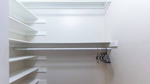 Ein begehbarer Kleiderschrank mit weißen Regalen und einer Kleiderstange.