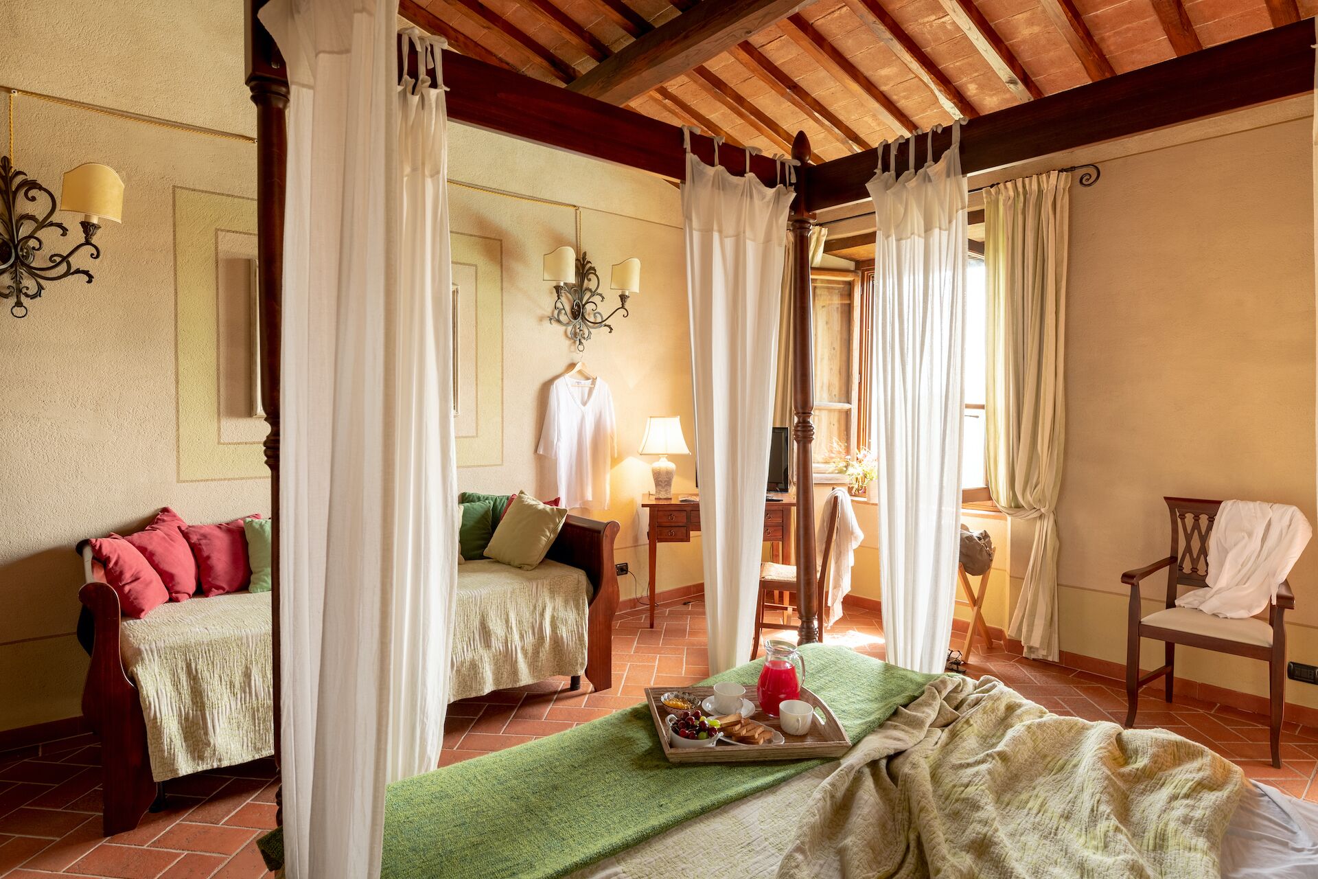 A bedroom with a four-poster bed, a second bed, a chair, a table with a lamp, and a tray with breakfast items.