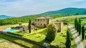 A stone villa with a swimming pool, surrounded by well-maintained lawns and cypress trees.