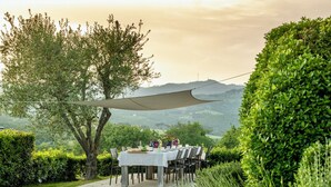 An outdoor dining area with a table set for guests, surrounded by lush greenery and a scenic mountain backdrop.