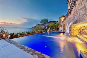 Ein Infinity-Pool mit Blick auf das Meer und ein Steinhaus mit einem Wasserfall.