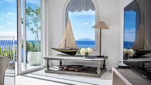 Een kamer met uitzicht op zee, een model zeilboot, een lamp en een tafel met bloemen.