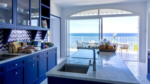 Een moderne keuken met blauwe kastjes en een groot raam met uitzicht op de oceaan.