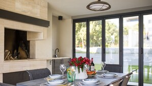 A modern dining area with a large table set for four, a fireplace, and a view of the outdoors through large windows.