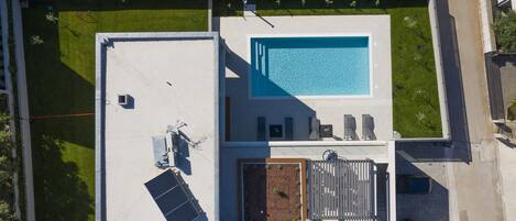 An aerial view of a rooftop with a swimming pool, a garden area, and a covered patio with seating.
