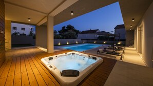 A hot tub on a wooden deck with a pool in the background.