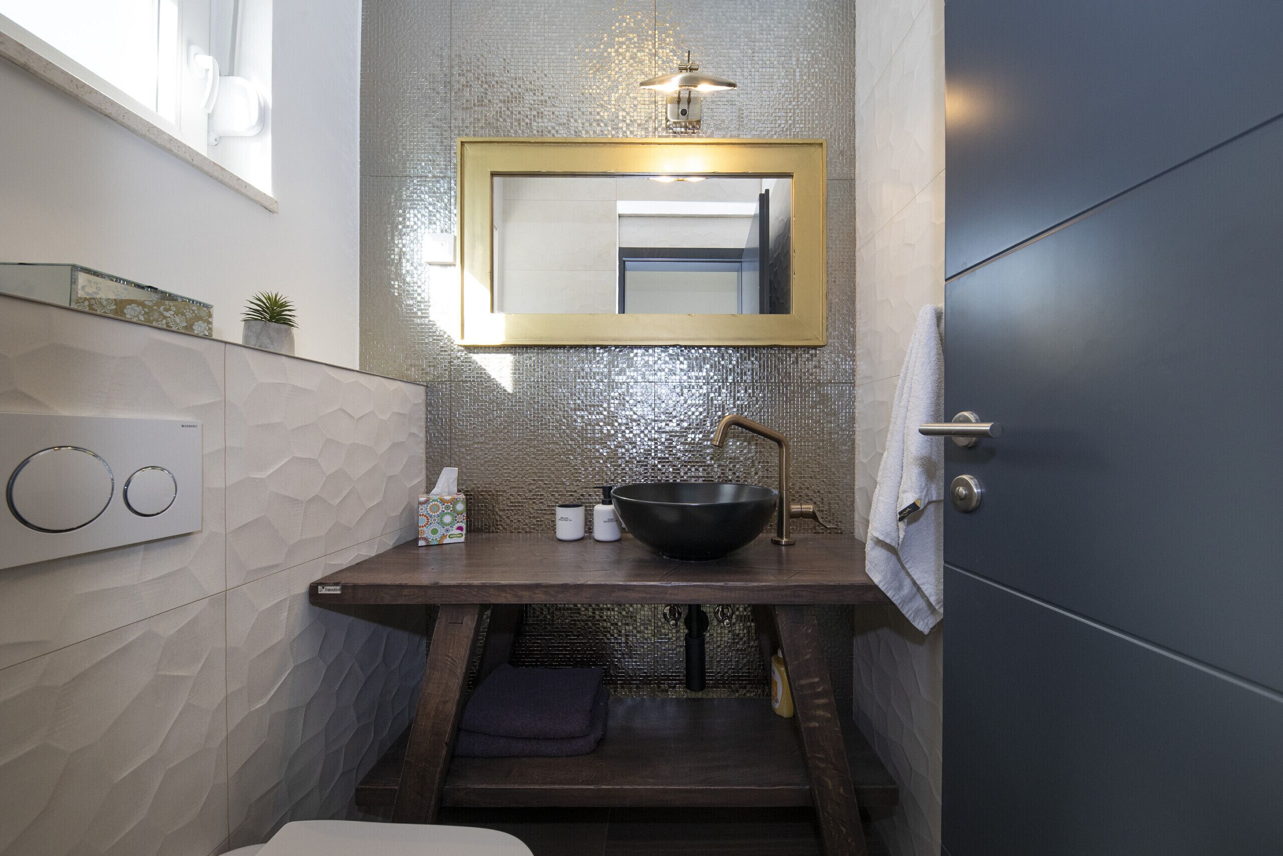 A modern bathroom with a large mirror, a black sink, and a towel rack.