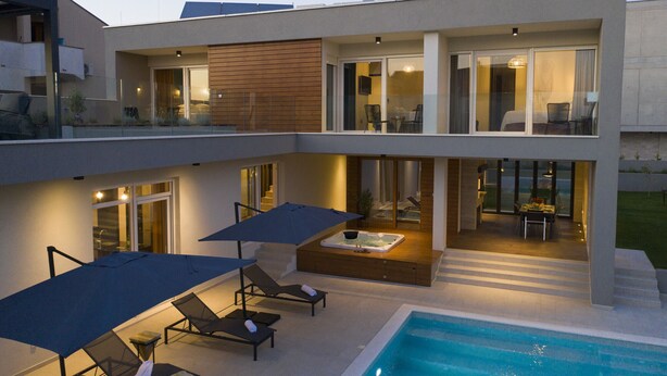 A modern two-story house with a swimming pool, outdoor seating, and a hot tub.