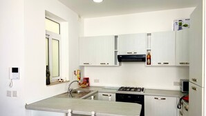 A compact kitchen with white cabinets, a gas stove, a dishwasher, and a small window.