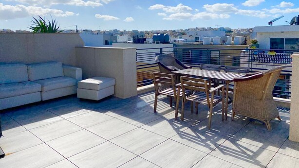 A rooftop terrace with a sofa, chairs, and a table.