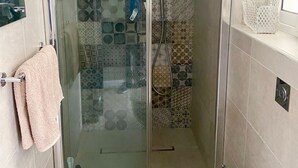 A modern bathroom with a glass-enclosed shower, patterned tiles, a toilet, and a towel rack.