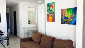 A modern living room with a brown sectional sofa, a dining area with a white table and chairs, and a kitchen in the background.