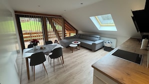 A modern loft apartment with a dining area, a gray sofa, a small round table, and a kitchen with a wooden countertop. - Recreation in the forest - with swimming pool! (Heßles)