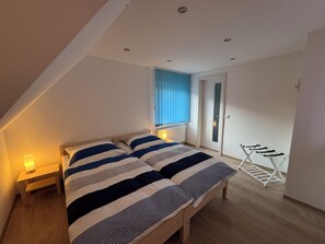 Ein Schlafzimmer mit Bett, Nachttischlampen, einem Fenster mit Jalousien, einer Tür und einem Wäscheständer.