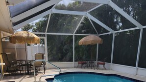 A swimming pool with a glass enclosure, surrounded by lounge chairs and a table. - Charming 3-bedroom house in quaint Venice with heated pool! (Venice)