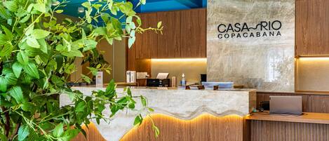 A reception desk with a marble top, wooden paneling, and a sign reading "CASA RIO COPACABANA".