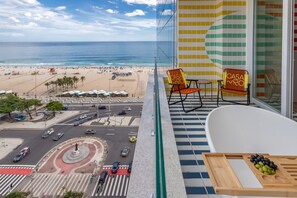 A balcony with a view of a beach and ocean, two chairs with a sign, and a bathtub with a tray and grapes.