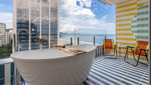 A modern bathroom with a freestanding bathtub, a large window overlooking the beach, and a tiled floor with a blue and white pattern.