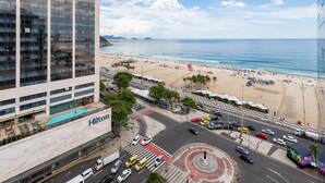 A hotel with a swimming pool, a beach, and a busy street with cars and taxis.