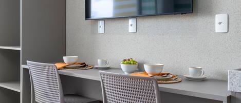 Ein moderner Essbereich mit einem an der Wand befestigten Flachbildfernseher, zwei Stühlen, einem Tisch mit Schüsseln und Tassen sowie Holzboden.