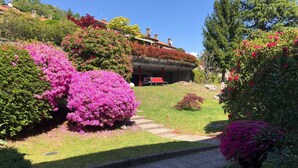 Een tuin met roze bloemen, een pad en een gebouw met een rode bank.